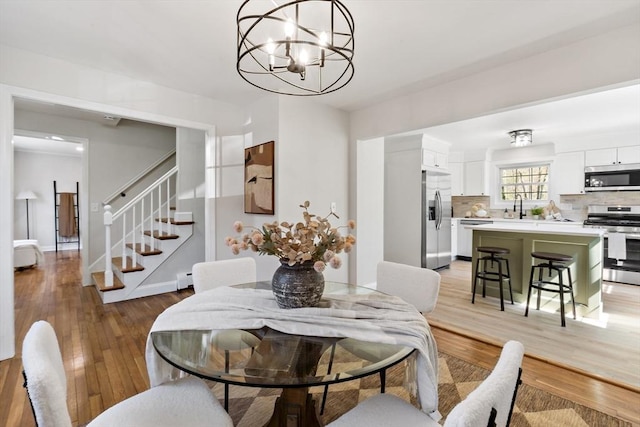 dining space featuring an inviting chandelier, light wood-style flooring, stairway, and a baseboard radiator