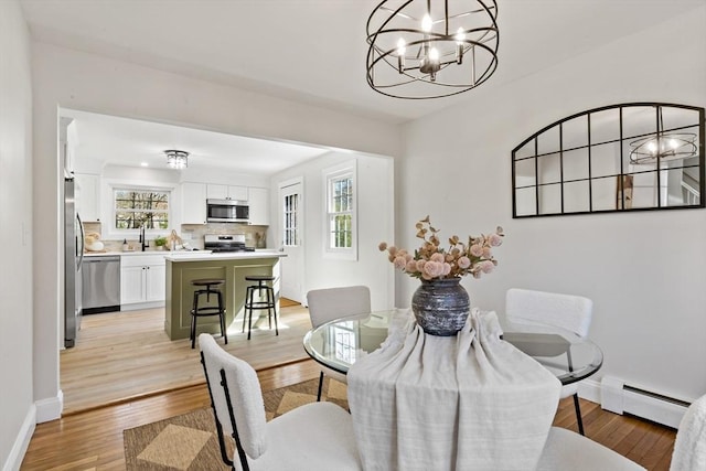 dining space with an inviting chandelier, baseboards, light wood finished floors, and a baseboard heating unit