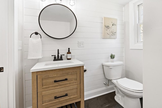 half bathroom featuring vanity, baseboards, wood walls, and toilet