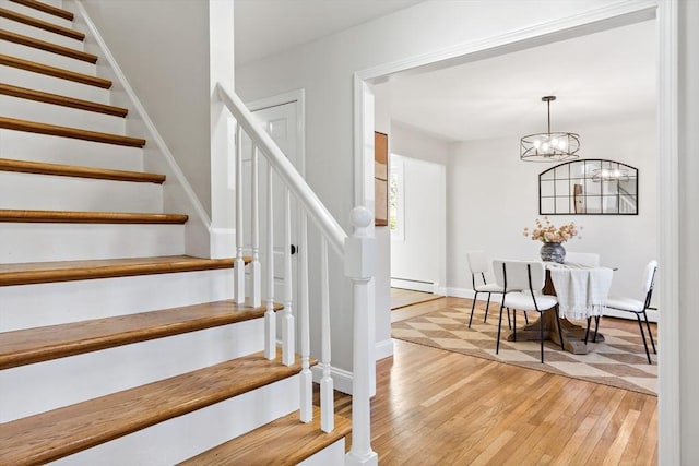 stairs with wood-type flooring, baseboards, a baseboard heating unit, and an inviting chandelier