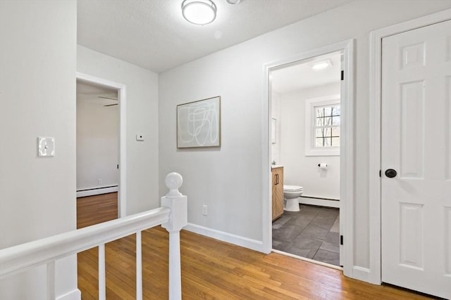 corridor with baseboards, a baseboard radiator, light wood-style flooring, and an upstairs landing