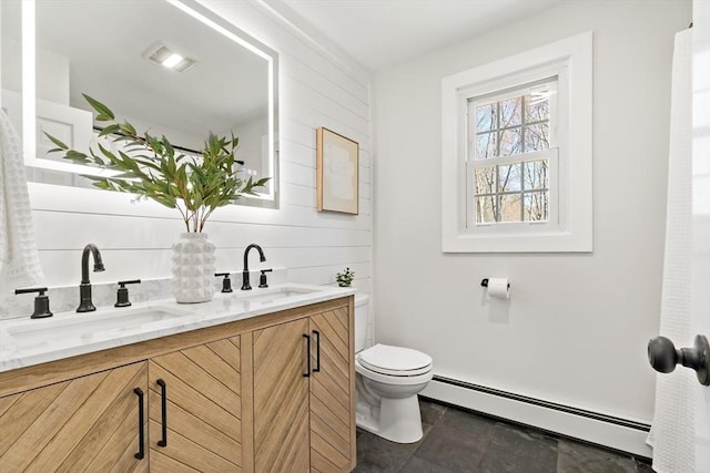 bathroom featuring double vanity, a sink, baseboard heating, and toilet