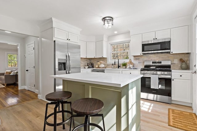 kitchen with decorative backsplash, a kitchen bar, light countertops, white cabinets, and appliances with stainless steel finishes