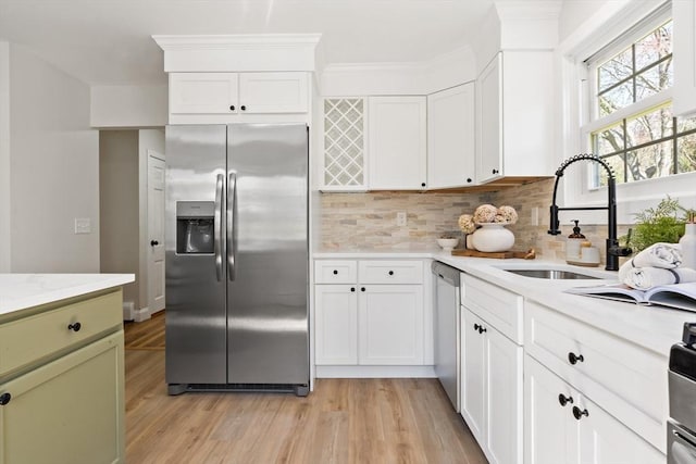 kitchen with backsplash, a sink, white cabinets, light wood finished floors, and stainless steel appliances