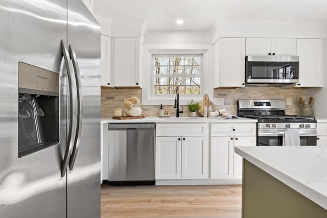 kitchen with decorative backsplash, appliances with stainless steel finishes, light wood-type flooring, a sink, and white cabinets