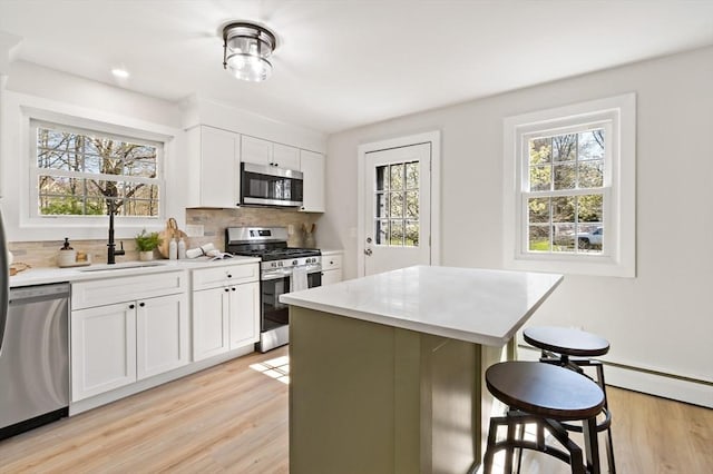 kitchen featuring a kitchen breakfast bar, light countertops, a sink, light wood finished floors, and appliances with stainless steel finishes