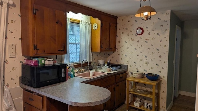 kitchen featuring wallpapered walls, black microwave, light countertops, brown cabinetry, and a sink