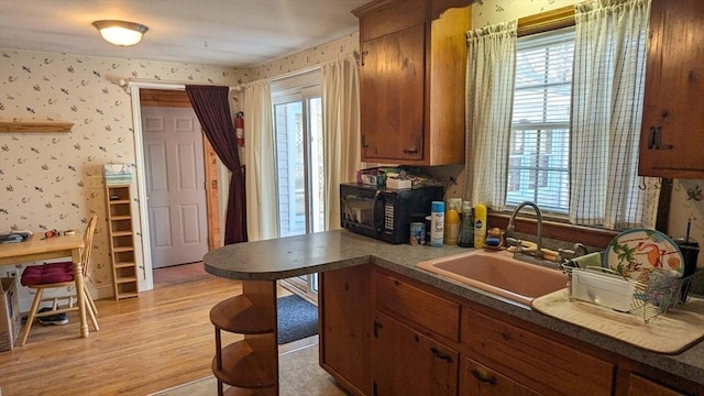 kitchen with light wood-style flooring, a sink, wallpapered walls, brown cabinetry, and black microwave