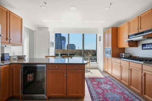 kitchen with gas stovetop, stainless steel microwave, a peninsula, under cabinet range hood, and wine cooler