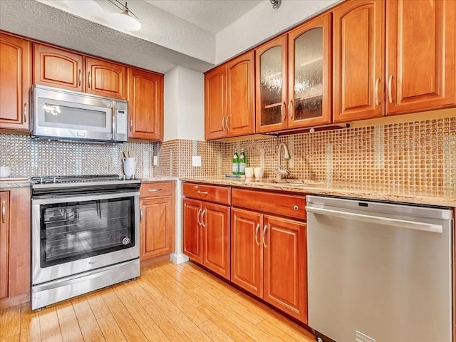 kitchen with brown cabinets, light stone countertops, stainless steel appliances, light wood-type flooring, and a sink