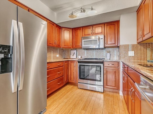 kitchen with stainless steel appliances, brown cabinetry, decorative backsplash, and light wood finished floors