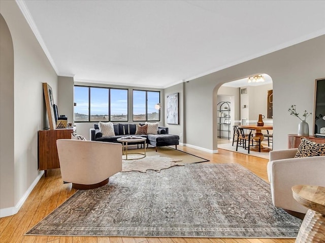 living room featuring light wood finished floors, baseboards, arched walkways, and crown molding