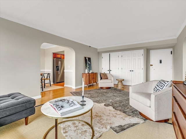 living area with ornamental molding, arched walkways, light wood-style flooring, and baseboards