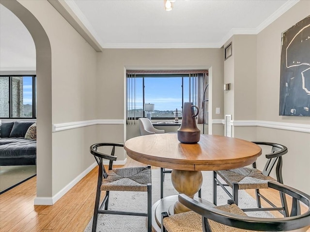 dining space featuring light wood-type flooring, a healthy amount of sunlight, arched walkways, and crown molding