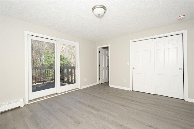 unfurnished bedroom featuring access to exterior, baseboard heating, dark hardwood / wood-style flooring, a textured ceiling, and a closet