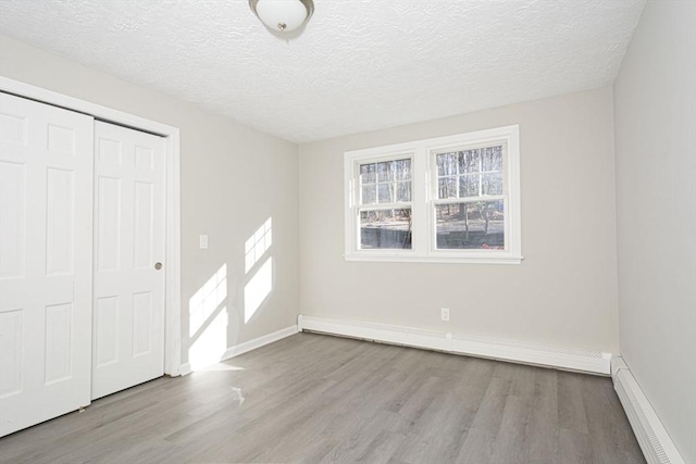 unfurnished bedroom featuring light hardwood / wood-style flooring, a textured ceiling, and a baseboard heating unit