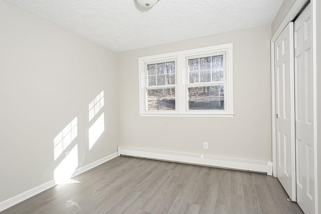 unfurnished bedroom featuring a textured ceiling, a closet, light hardwood / wood-style flooring, and a baseboard heating unit