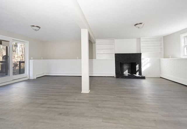 unfurnished living room with a fireplace, built in shelves, dark wood-type flooring, and brick wall