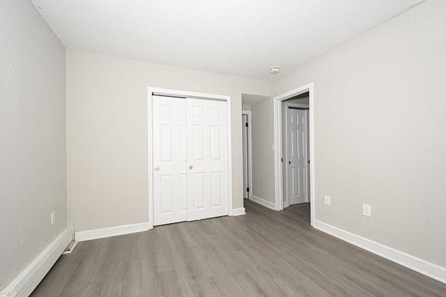 unfurnished bedroom with hardwood / wood-style floors, a closet, and baseboard heating