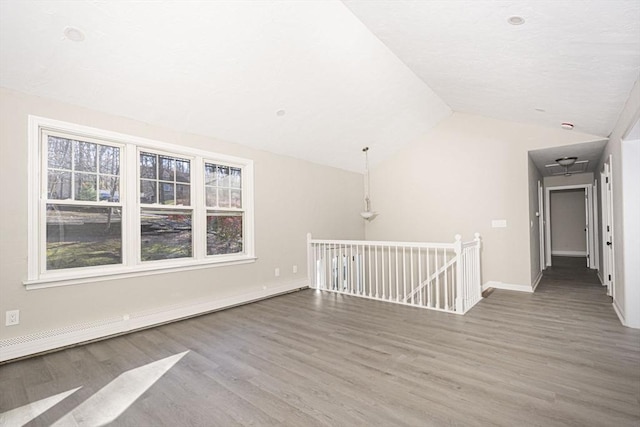 empty room featuring wood-type flooring, a baseboard radiator, and vaulted ceiling