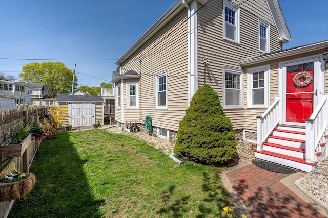 view of side of home featuring fence, a shed, entry steps, an outbuilding, and a lawn