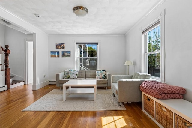 living area featuring a healthy amount of sunlight, crown molding, stairway, and a baseboard heating unit