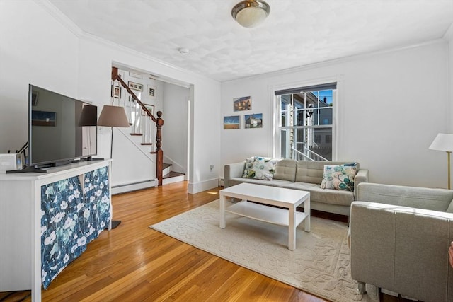 living area featuring baseboard heating, baseboards, light wood-style floors, ornamental molding, and stairs