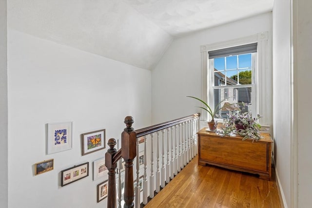 corridor featuring baseboards, an upstairs landing, wood finished floors, and lofted ceiling