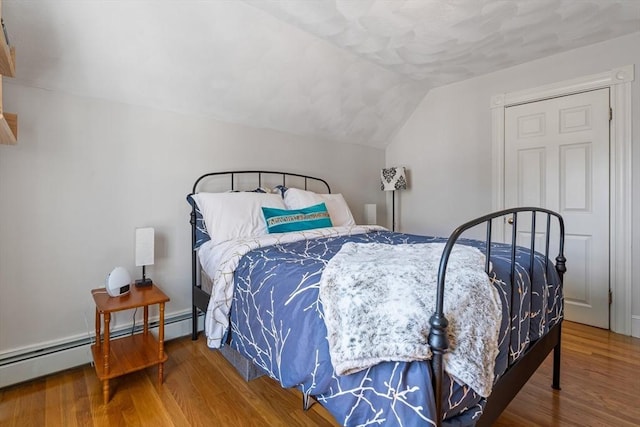 bedroom with a baseboard heating unit, wood finished floors, and lofted ceiling