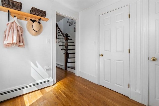 foyer with wood finished floors, baseboard heating, and stairway