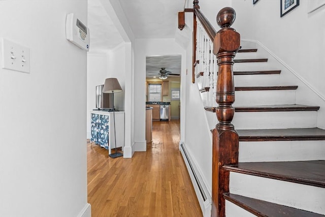 stairway with baseboards, ceiling fan, baseboard heating, and wood finished floors