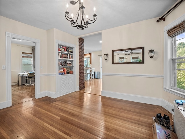 unfurnished dining area with a notable chandelier, a wealth of natural light, built in features, and hardwood / wood-style flooring