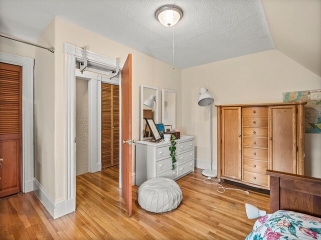 bedroom with a textured ceiling, light hardwood / wood-style flooring, and vaulted ceiling