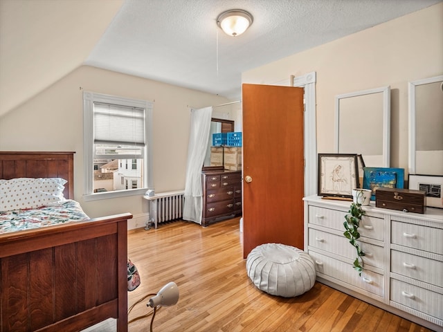 bedroom featuring a textured ceiling, lofted ceiling, light hardwood / wood-style floors, and radiator heating unit