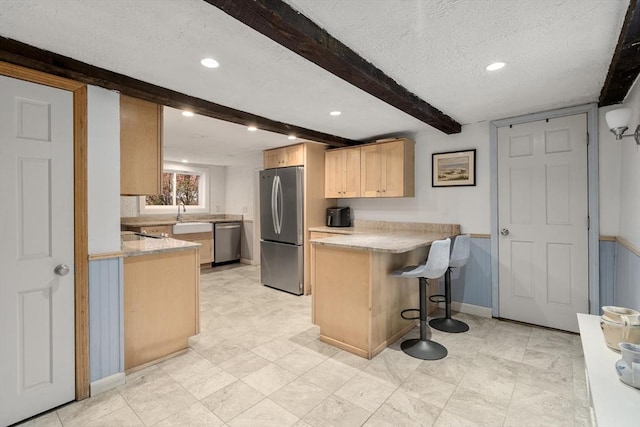 kitchen with a peninsula, light brown cabinets, beamed ceiling, light countertops, and stainless steel appliances