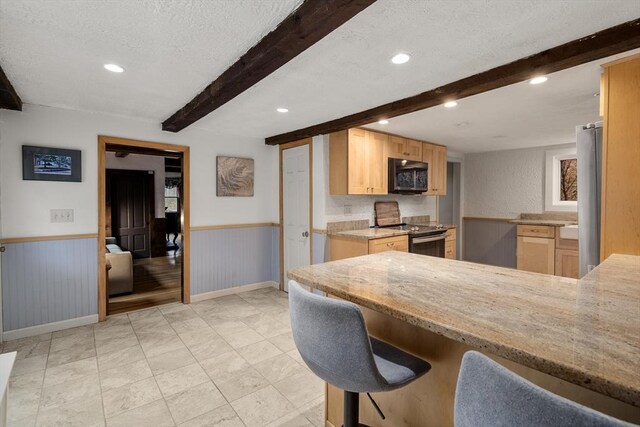 kitchen featuring beamed ceiling, wainscoting, black appliances, and light brown cabinets
