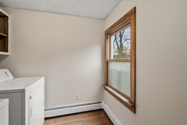 clothes washing area featuring washing machine and clothes dryer, laundry area, wood finished floors, and a baseboard radiator