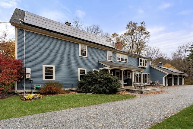 rear view of house with gravel driveway, a chimney, and solar panels