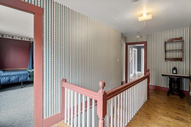 hallway featuring an upstairs landing, hardwood / wood-style floors, and wallpapered walls