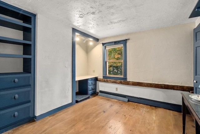 unfurnished bedroom with a baseboard heating unit, light wood finished floors, and a textured ceiling