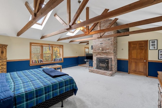 bedroom with wainscoting, a brick fireplace, beam ceiling, carpet flooring, and a skylight