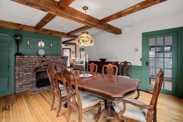 dining space with light wood-style flooring, a fireplace, and beamed ceiling