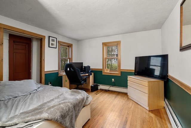 bedroom with a baseboard heating unit, multiple windows, and light wood-style flooring