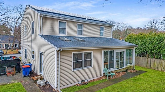 rear view of property featuring a yard and solar panels