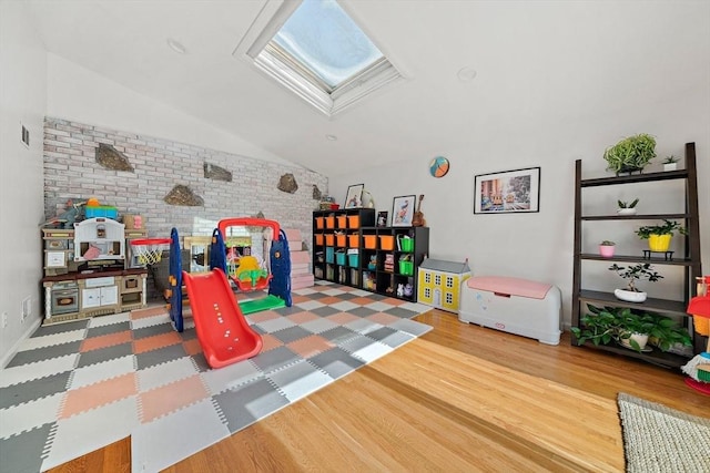 recreation room featuring brick wall, vaulted ceiling with skylight, and wood finished floors