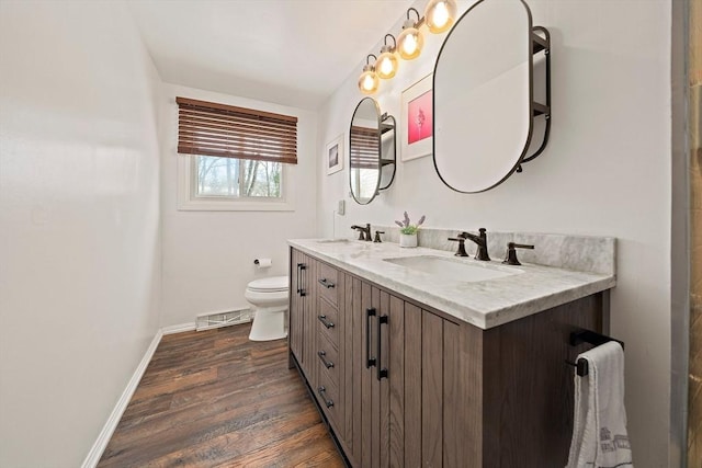 bathroom with toilet, wood finished floors, visible vents, a sink, and baseboards