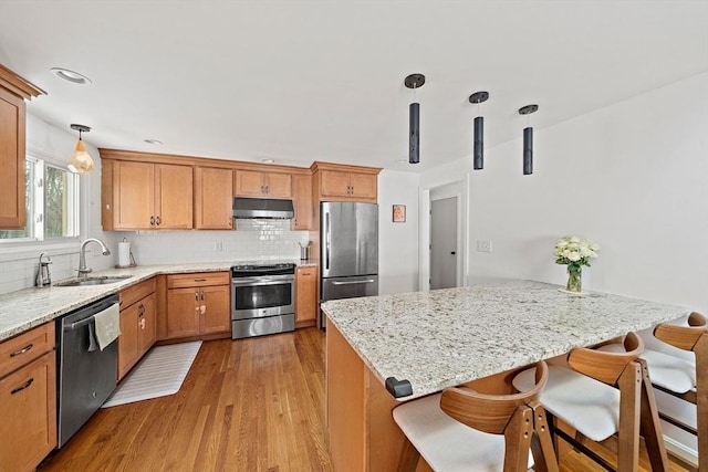 kitchen featuring under cabinet range hood, a sink, appliances with stainless steel finishes, tasteful backsplash, and decorative light fixtures