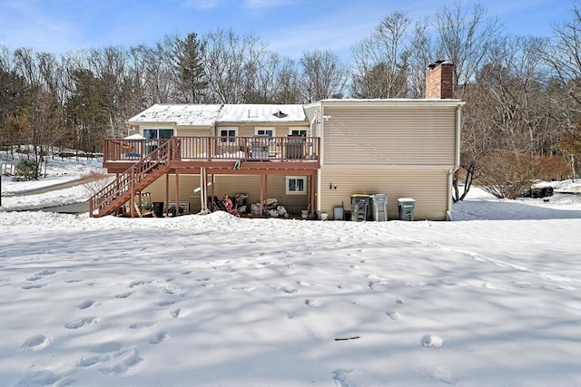 snow covered property with a deck, a chimney, and stairs