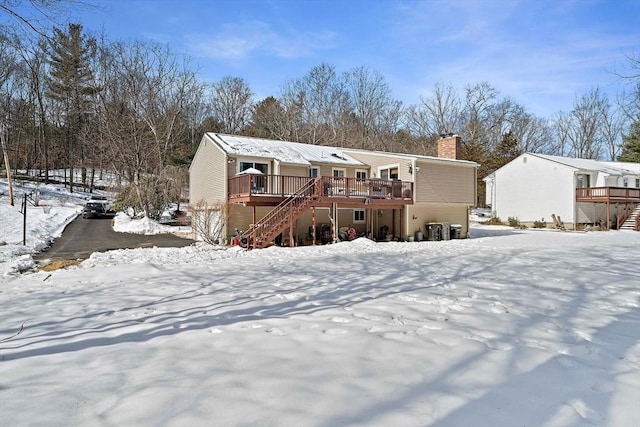 snow covered back of property with a chimney, a deck, and stairs