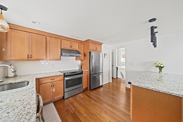 kitchen with stainless steel appliances, hanging light fixtures, a sink, and under cabinet range hood